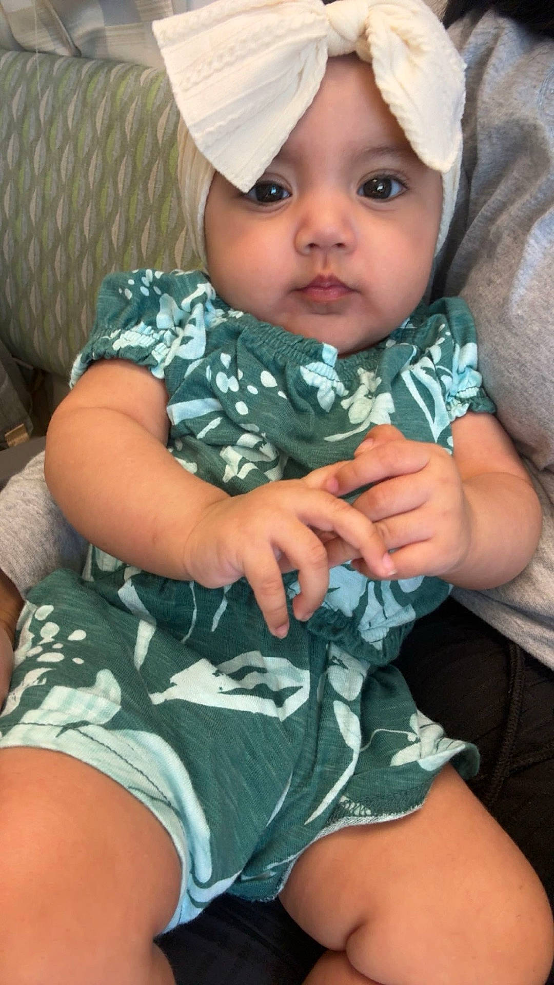 Elsy is registered to the contest to win money with this photo: arm, baby, bow, child, cute, eyes, face, green_clothing, hands, headband, indoor, infant, lap, legs, mouth, patterned_outfit, person, sitting, skin, young_child