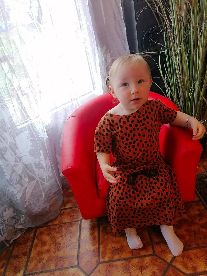 Latiana participe au concours pour gagner de l'argent avec cette photo : baby, baby_toddler_clothing, child, comfort, curtain, dress, eye, face, floor, flooring, hairstyle, human_leg, pattern, person, skin, sleeve, textile, thigh, toddler, window