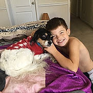Wallie is registered to the contest to win money with this photo: boy, dog, pet, child, smiling, bed, blanket, indoor, happy, canine, fur, cute, red_sweater, carpet, home, portrait, love, affection, comfort, cozy