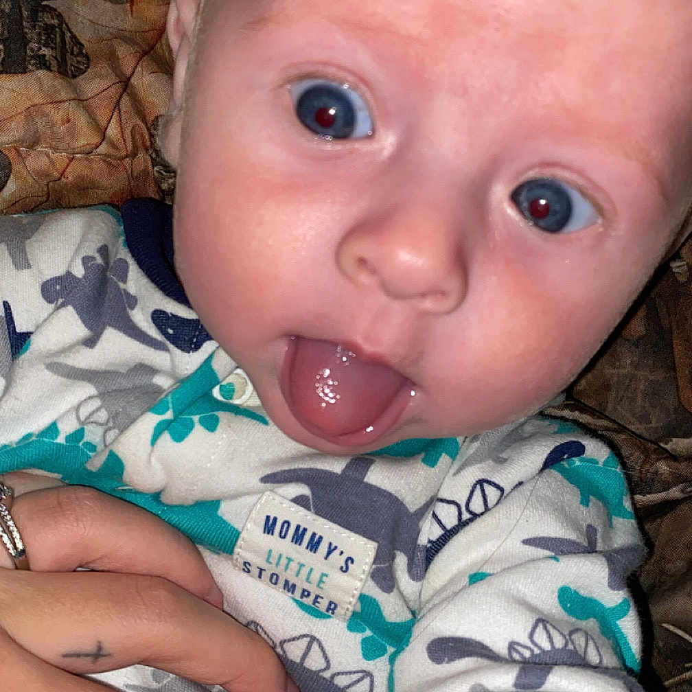 Carter joined the competition — help win amazing prizes! baby, bodypart, clothing, couch, cushion, face, finger, furniture, hand, head, homedecor, mouth, newborn, person, photography, portrait, quilt, selfie, t_shirt, tongue