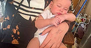 Maddox is registered to the contest to win money with this photo: baby, background_items, casual_clothing, closeup, hand, holding, hoodie, indoor, infant, logo, nails, peaceful, person, portrait, relaxed, rosy_cheeks, seated, sleeping, tie_dye, wooden_chair