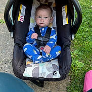 Maddox is registered to the contest to win money with this photo: baby, car_seat, pajamas, blue_clothing, outdoor, grass, concrete, infant, child, seat_belt, person, footwear, sunlight, nature, warning_label, serious_expression, sitting, head, face, cute