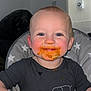 baby, child, messy_face, high_chair, food, orange_food, smile, blue_eyes, short_hair, black_clothing, elephant_print, hand, indoor, kitchen, feeding, cute, happy, toddler, face, messy