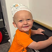 Nolan is registered to the contest to win money with this photo: toddler, child, smile, orange_clothing, diaper, indoor, stroller, holding, happy, cute, carpet, wall, baby, playful, person, headwear, blue_eyes, small_person, fun, infant