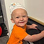 toddler, child, smile, orange_clothing, diaper, indoor, stroller, holding, happy, cute, carpet, wall, baby, playful, person, headwear, blue_eyes, small_person, fun, infant