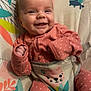 baby, smiling, infant, pink_clothing, polka_dot, baby_seat, colorful, animal_print, leaf_pattern, happy, cute, child, portrait, indoors, cozy, soft_fabric, playful, small_hands, relaxed, seated