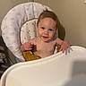 Leilani is registered to the contest to win money with this photo: baby, child, infant, high_chair, smiling, portrait, indoor, home, kitchen, seated, face, eyes, hair, hands, bare_arms, tray, chair, cushion, rainbow_pattern, happy