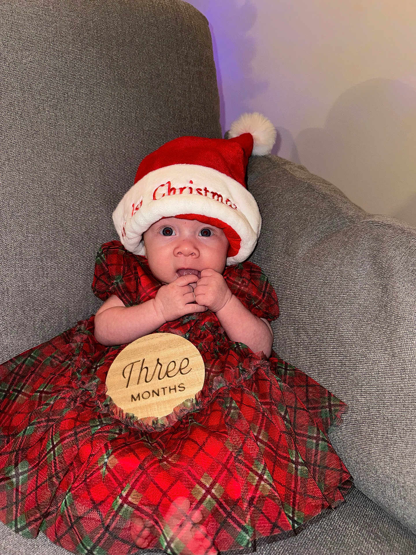 Leilani joined the competition — help win amazing prizes! baby, infant, child, santa_hat, christmas, holiday, plaid_dress, red_dress, milestone_sign, three_months, wooden_sign, couch, sofa, portrait, indoor, hands_near_mouth, big_eyes, cute, festive, hat_pom_pom