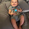 baby, smiling, infant, onesie, gray, perfume_bottle, blue_cap, cushion, soft_fabric, sitting, happy, child, portrait, indoors, cute, young, skin, person, hand, foot