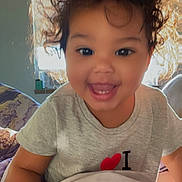 Harmonii joined the competition — help win amazing prizes! toddler, child, smiling, portrait, indoor, bedroom, bed, blanket, bedding, curly_hair, happy, face, person, sitting, casual_clothing, gray_shirt, sunlight, window, cozy, morning