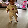Harmonii is registered to the contest to win money with this photo: toddler, child, baby, smiling, standing, indoors, portrait, bow, curly_hair, jumpsuit, sneakers, rainbow, toy, playpen, nursery, floor, window, furniture, happy, walking