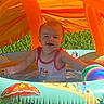 baby, child, infant, smiling, outdoor, summer, swimming_pool, inflatable_pool, water, beach_ball, orange, grass, backyard, playtime, sitting, tank_top, cartoon, sunlight, portrait, happy