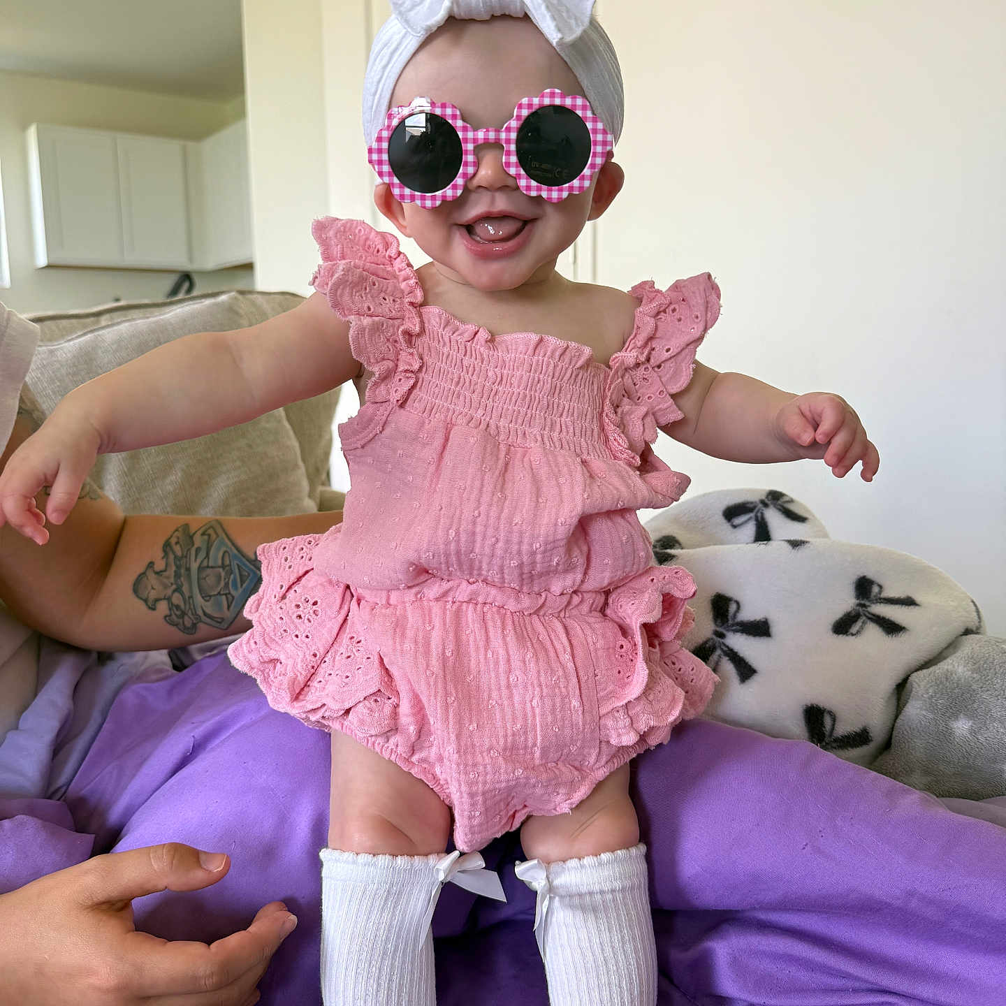 Kayslynn is registered to the contest to win money with this photo: accessories, baby, child, clothing, couch, cute, happy, headband, home, indoor, infant, person, pink_outfit, purple_blanket, sitting, smiling, sunglasses, tattoo, white_bow, white_socks