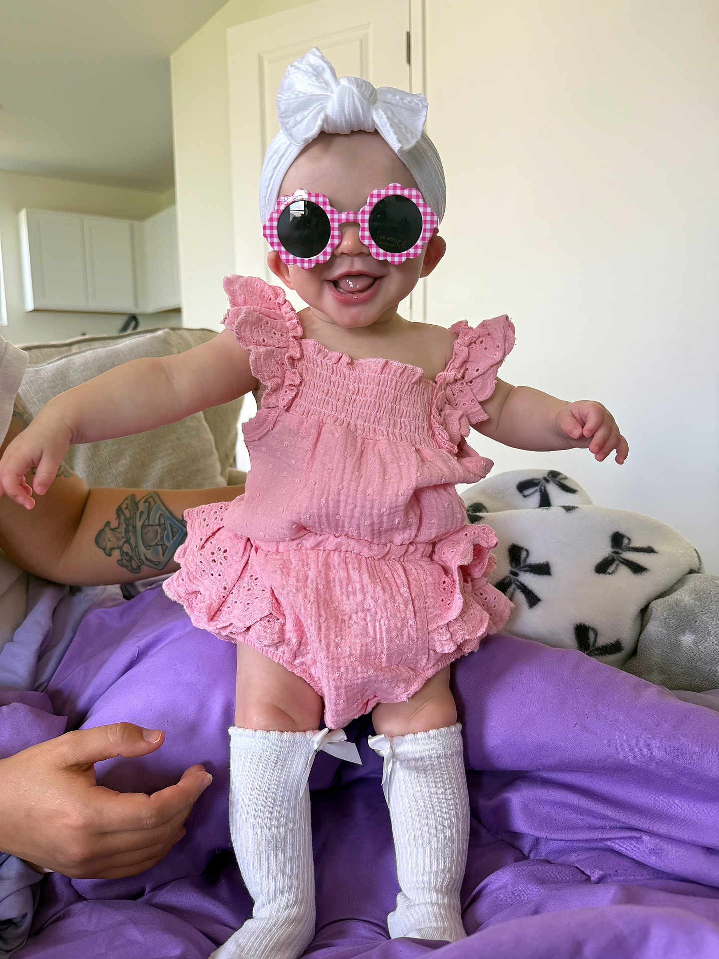 Kayslynn is registered to the contest to win money with this photo: baby, pink_outfit, sunglasses, headband, white_bow, smiling, sitting, tattoo, purple_blanket, couch, indoor, person, child, cute, happy, white_socks, infant, clothing, accessories, home