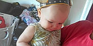 Joey joined the competition — help win amazing prizes! baby, child, viking_helmet, person, indoor, clothing, curious, holding, sports_jersey, wall_hanging, pile_of_clothes, pink_shirt, face, headwear, playful, room, carpet, furniture, casual, portrait