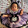 baby, child, costume, purple, black, cat_ears, headband, floral_blanket, cute, infant, smile, face, clothing, lying_down, indoors, person, adorable, soft, pink_flowers, ribbons