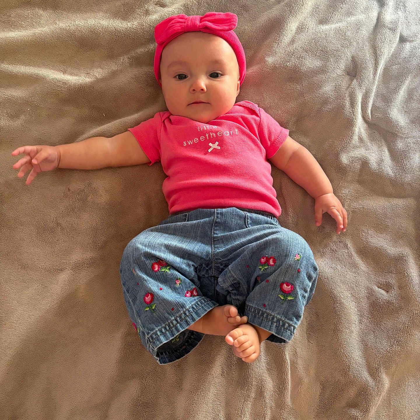 Mayssa joined the competition — help win amazing prizes! baby, infant, child, pink_headband, pink_shirt, jeans, embroidery, barefoot, blanket, soft_texture, lying_down, cute, adorable, portrait, indoor, playful, young_child, clothing, expression, person