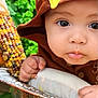 Mathias is registered to the contest to win money with this photo: baby, child, face, hand, brown_hood, yellow_patch, metal_tray, lettuce, corn, vegetables, closeup, cute, infant, outdoor, fresh, food, portrait, curious, small_hands, natural_light