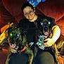 arm, black_dog, blanket, brindle_dog, collar, couch, cozy, dog, flash_glare, glasses, indoor, lap, living_room, person, pet_owner, red_eye, sitting, smiling, tongue_out, two_dogs