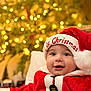 Lucca is registered to the contest to win money with this photo: baby, child, santa_hat, christmas, holiday, festive, smile, face, portrait, red_clothing, white_fur, button, indoor, lights, bokeh, celebration, cute, seasonal, happy, infant