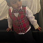 Zyaire is registered to the contest to win money with this photo: child, toddler, plaid_vest, bowtie, white_shirt, black_pants, indoor, couch, carpet, curly_hair, earring, portrait, leaning, casual_pose, furniture, blanket, soft_lighting, thoughtful, young_person, clothing