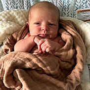 Wyatt is registered to the contest to win money with this photo: baby, blanket, infant, face, wrapped, cushion, patterned_background, soft_texture, cozy, seated, newborn, skin, head, hands, expression, indoors, portrait, closeup, child, warm