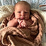 baby, blanket, infant, face, wrapped, cushion, patterned_background, soft_texture, cozy, seated, newborn, skin, head, hands, expression, indoors, portrait, closeup, child, warm