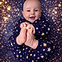 baby, background_bokeh, blue_clothing, child, close_up, cute, expression, face, feet, hands, happy, indoor, infant, pajamas, playful, portrait, skin, smiling, soft_lighting, stars