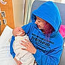 Maddox is registered to the contest to win money with this photo: baby, child, hospital, person, blue_hoodie, pink_hair, blanket, medical_tube, cradle, smile, seated, indoor, bed, medical_equipment, face, hand, young_person, curtain, comfort, care