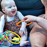 Nova joined the competition — help win amazing prizes! adult, baby, baby_carrier, blue_blanket, child, closeup, colorful_toys, family, happy, indoor, infant, laughing, leopard_print, onesie, orange_ring, playtime, portrait, sitting, smiling, toy