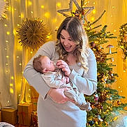Noah participe au concours pour gagner de l'argent avec cette photo : woman, baby, child, christmas_tree, holiday_lights, gift_boxes, cozy_clothing, indoor, smiling, decorations, festive, warm_lighting, family, holding, toddler, celebration, home_decor, portrait, seasonal, happy