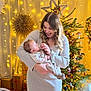 woman, baby, child, christmas_tree, holiday_lights, gift_boxes, cozy_clothing, indoor, smiling, decorations, festive, warm_lighting, family, holding, toddler, celebration, home_decor, portrait, seasonal, happy