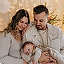 Noah participe au concours pour gagner de l'argent avec cette photo : family, baby, adult, woman, man, holding, pacifier, clothing, indoor, fairy_lights, decorations, christmas_tree, warm_lighting, portrait, love, togetherness, smile, cozy, holiday, parenting