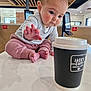 Amelie is registered to the contest to win money with this photo: baby, infant, table, coffee_cup, drool, cafe, indoor, curious, reaching_hand, pink_pants, striped_shirt, face, feet, wood_ceiling, digital_screens, window, light, person, expression, cute