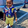Demetrius is registered to the contest to win money with this photo: toddler, child, smiling, braided_hair, hawaiian_shirt, yellow_shorts, sneakers, watch, parking_lot, car, shadow, outdoor, sunny, happy, fashion, person, standing, casual_clothing, daylight, cute