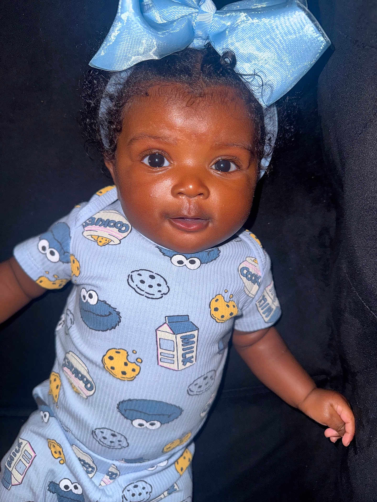 Daige Dior joined the competition — help win amazing prizes! baby, child, face, headband, blue_bow, onesie, cookie_monster, milk_carton, cookie, curly_hair, dark_background, smile, portrait, infant, cute, clothing, person, closeup, indoors, happy