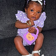 Daige Dior is registered to the contest to win money with this photo: baby, child, girl, purple_outfit, white_hearts, curly_hair, bows, bracelets, plush_purse, bear_face, white_sandals, couch, dark_background, sitting, cute, playful, curious, indoor, person, portrait