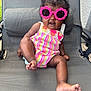 Daige Dior is registered to the contest to win money with this photo: baby, child, sunglasses, pink, flower_shaped, romper, striped, chair, outdoor, smiling, happy, cute, fashion, summer, playful, seat, feet, hand, person, portrait