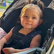 Paisley is registered to the contest to win money with this photo: toddler, child, baby, stroller, pigtails, hair, face, blue_eyes, smile, clothing, seatbelt, outdoor, sunlight, expression, hand, portrait, cute, person, infant, casual
