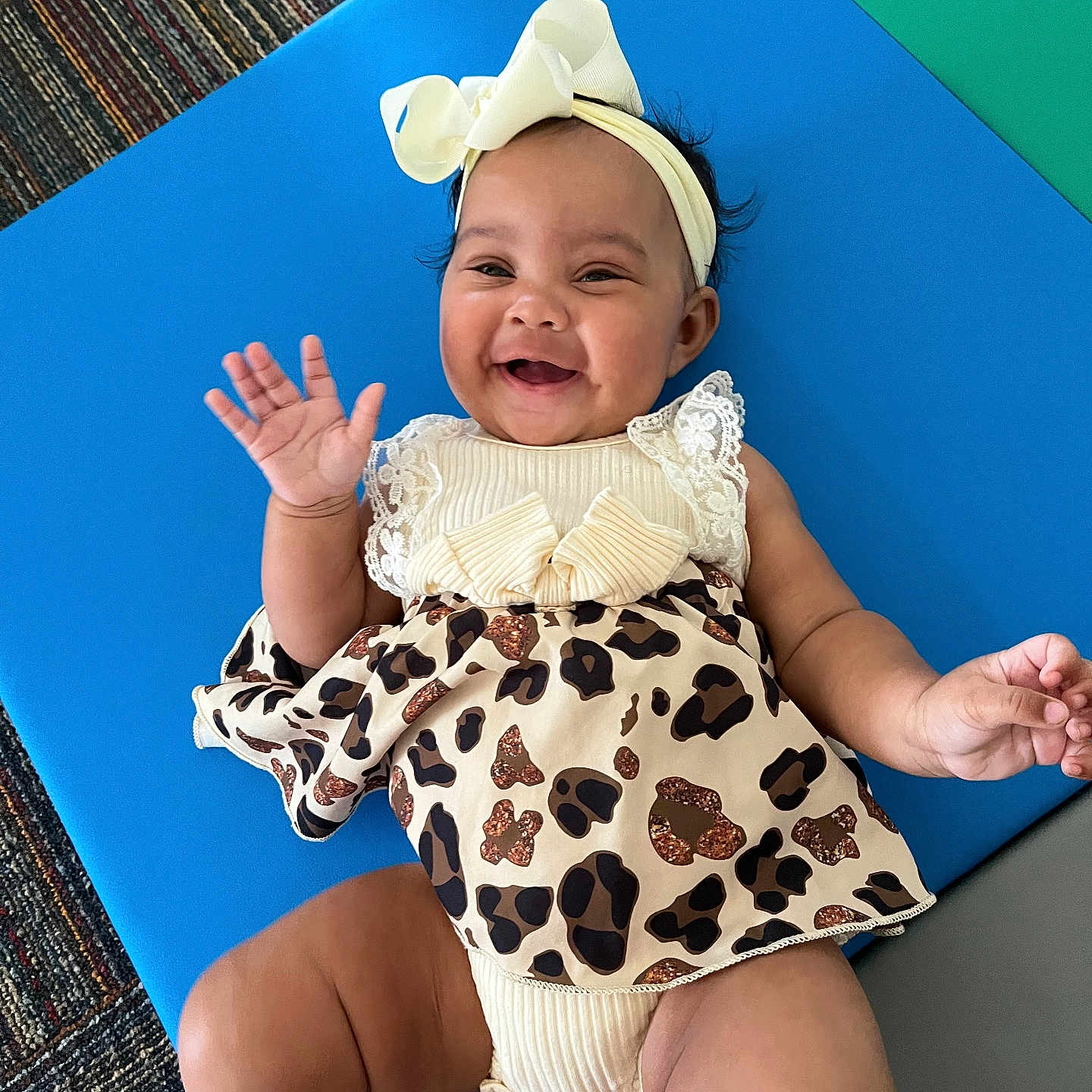 Annelaine is registered to the contest to win money with this photo: baby, baby_accessory, baby_girl, blue_mat, cheerful, child, clothing, crawling_mat, cute, cute_outfit, fashion, happy, headband, indoor, infant, leopard_print, person, portrait, smiling, waving