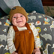 Sebastian joined the competition — help win amazing prizes! baby, child, smile, hat, knit_hat, overalls, brown_clothing, cushion, animal_pattern, lion, elephant, giraffe, bird, white_shirt, indoor, furniture, couch, pillow, happy, portrait