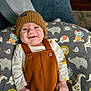 baby, child, smile, hat, knit_hat, overalls, brown_clothing, cushion, animal_pattern, lion, elephant, giraffe, bird, white_shirt, indoor, furniture, couch, pillow, happy, portrait