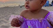 Saphira joined the competition — help win amazing prizes! baby, beach, child, colorful_clothing, curly_hair, floral_embroidery, happy, looking_away, ocean, outdoors, portrait, purple_dress, sand, seaside, shoreline, sitting, sunset, toddler, travel, tutu