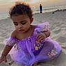 Saphira is registered to the contest to win money with this photo: child, toddler, baby, girl, portrait, beach, sand, sunset, ocean, shoreline, dress, purple_dress, floral_pattern, sitting, curly_hair, serious_expression, outdoor, seaside, beachgoer, photography
