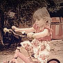 child, tricycle, outdoor, pink, flowered_skirt, short_sleeve_shirt, garden, leaves, bike, handlebars, footwear, young_child, curly_hair, play, summer_clothing, concrete_ground, toy, person, nature, daytime