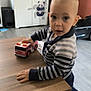 toddler, child, toy, fire_truck, table, striped_sweater, indoor, floor, cabinet, panda_decor, clothing, person, curious, play, wooden_table, shoes, home, furniture, expression, room