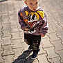 child, boy, hoodie, cartoon, outdoor, pavement, shadow, casual_clothing, sneakers, daylight, portrait, curious, standing, young, cute, expression, street, sunlight, fashion, casual