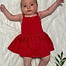baby, infant, red_dress, floral_blanket, lying_down, arms_outstretched, cute, child, portrait, indoors, skin, face, expression, feet, head, person, newborn, fabric, pattern, colorful