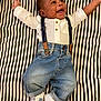 baby, infant, smiling, striped_blanket, white_shirt, suspenders, denim_jeans, sneakers, happy, lying_down, cute, child, portrait, casual_clothing, indoor, fashion, young_child, person, feet, hands