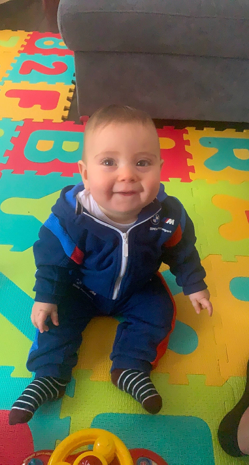 Raphaël a rejoint le concours — aidez-le/la à gagner de superbes lots ! baby, baby_toddler_clothing, child, clothing, electric_blue, facial_expression, flooring, fun, happy, joy, leisure, orange, pattern, person, play, recreation, room, sitting, smile, t_shirt